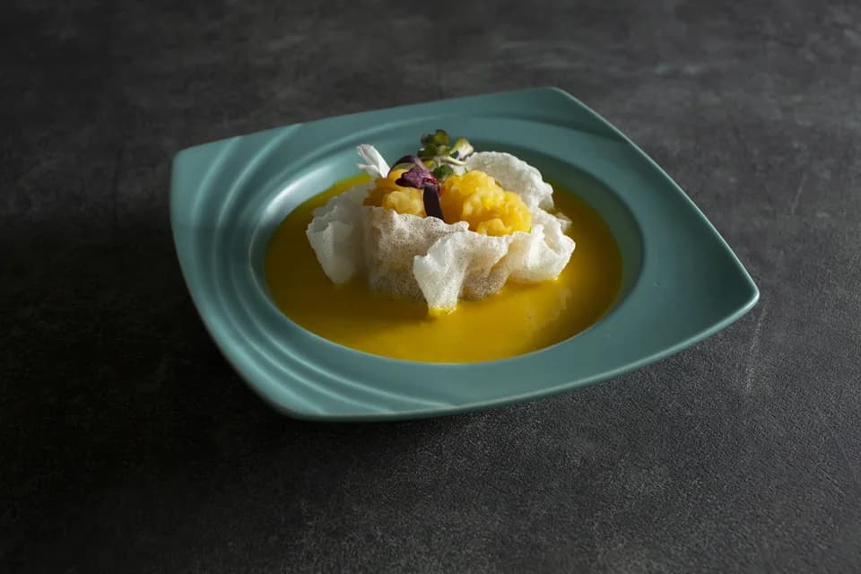 Golden pumpkin soup with crisp rice paper in a turquoise bowl