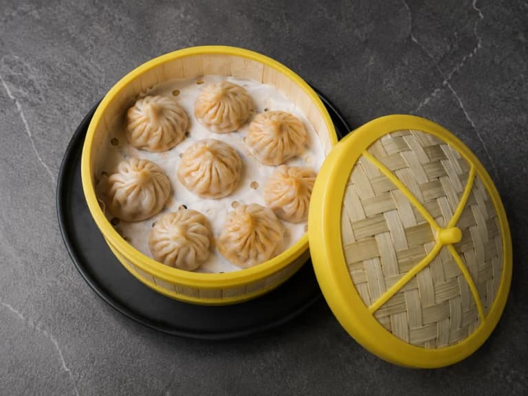 Handmade xiaolongbao in a yellow bamboo steamer